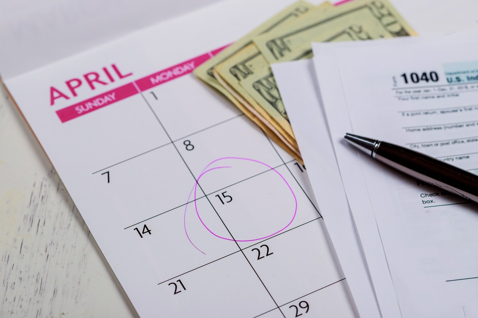 Calendar with words Tax Day , dollars and form 1040 income tax form showing tax day for April
